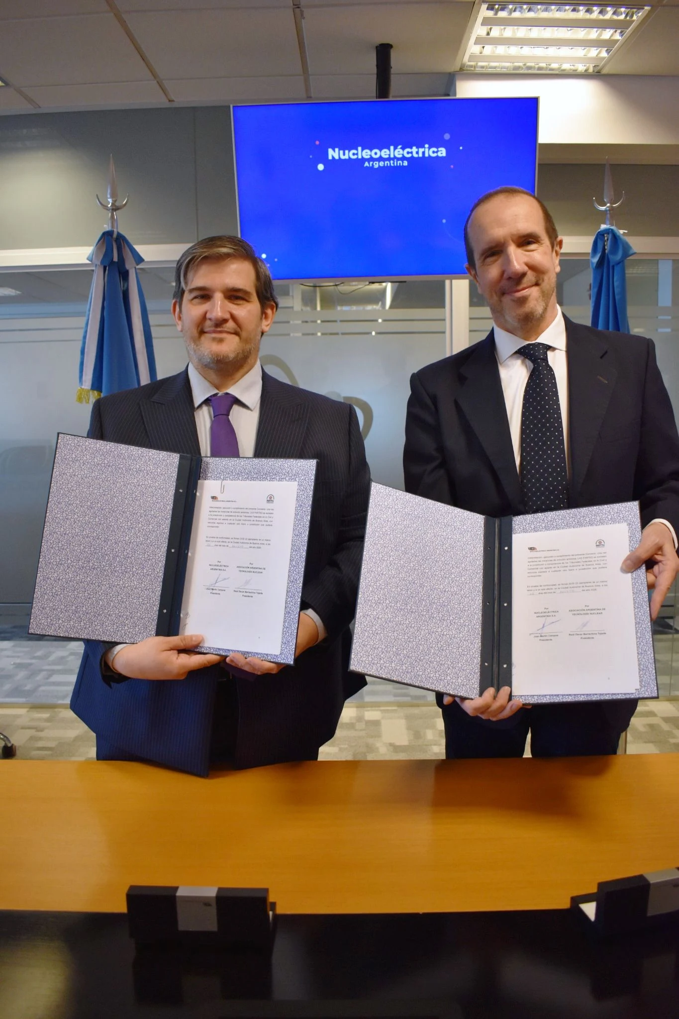 Representantes de Nucleoeléctrica Argentina y la AATN exhiben el convenio firmado ante una pantalla institucional.